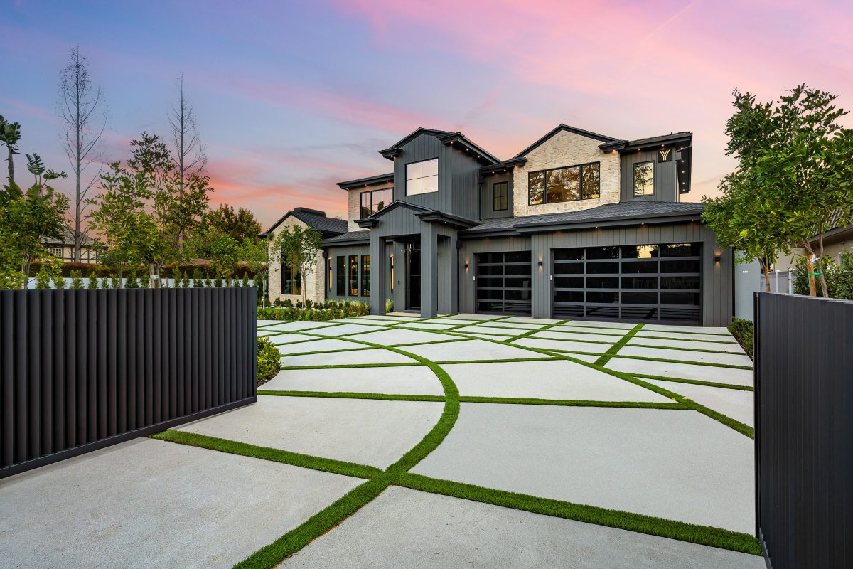 Modern two-story house with a beautifully designed driveway and lush greenery at sunset.